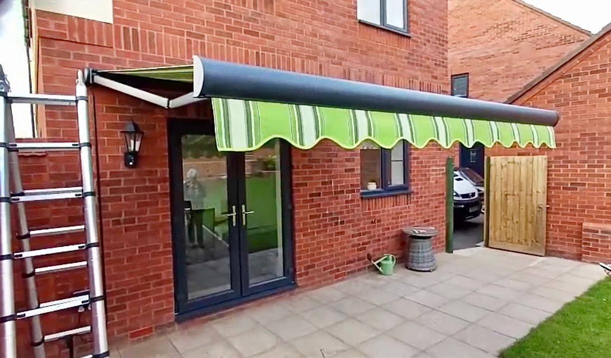 Green-striped retractable patio awning installed over bifold doors by Shires Shutters