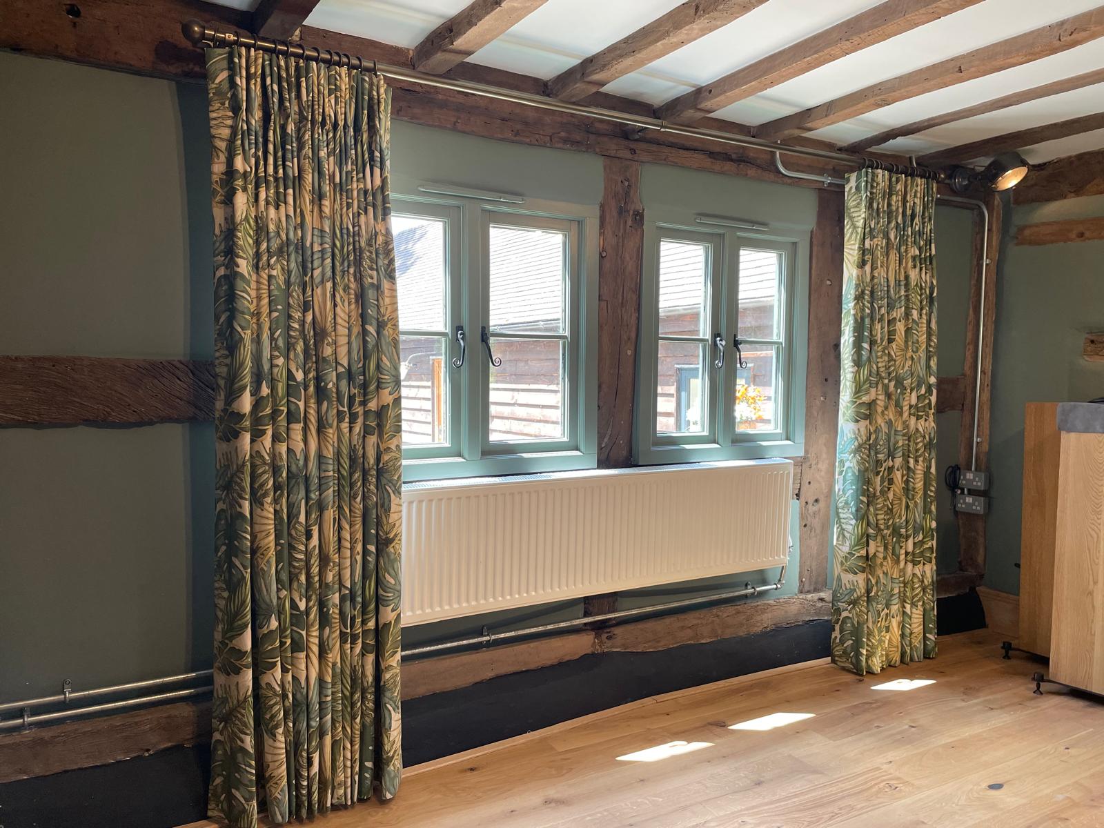 Floor length tropical leaf curtains in a beamed sage green room